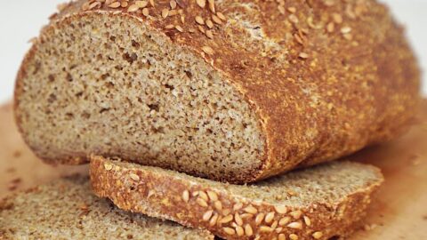 A loaf of homemade chickpea bread on a wooden board, with two slices cut