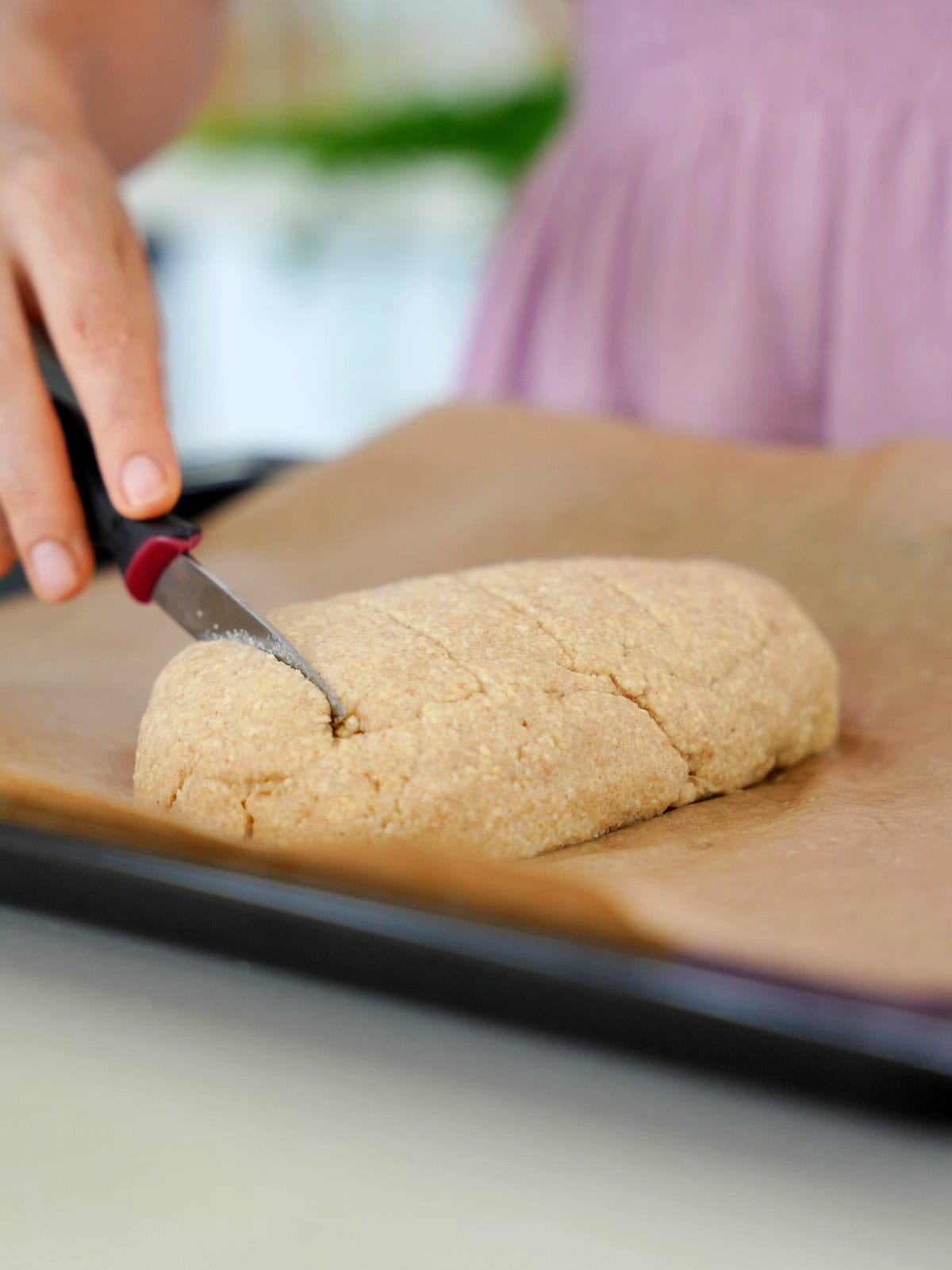 Elavegan scores unbaked bread loaf on a baking sheet with a knife
