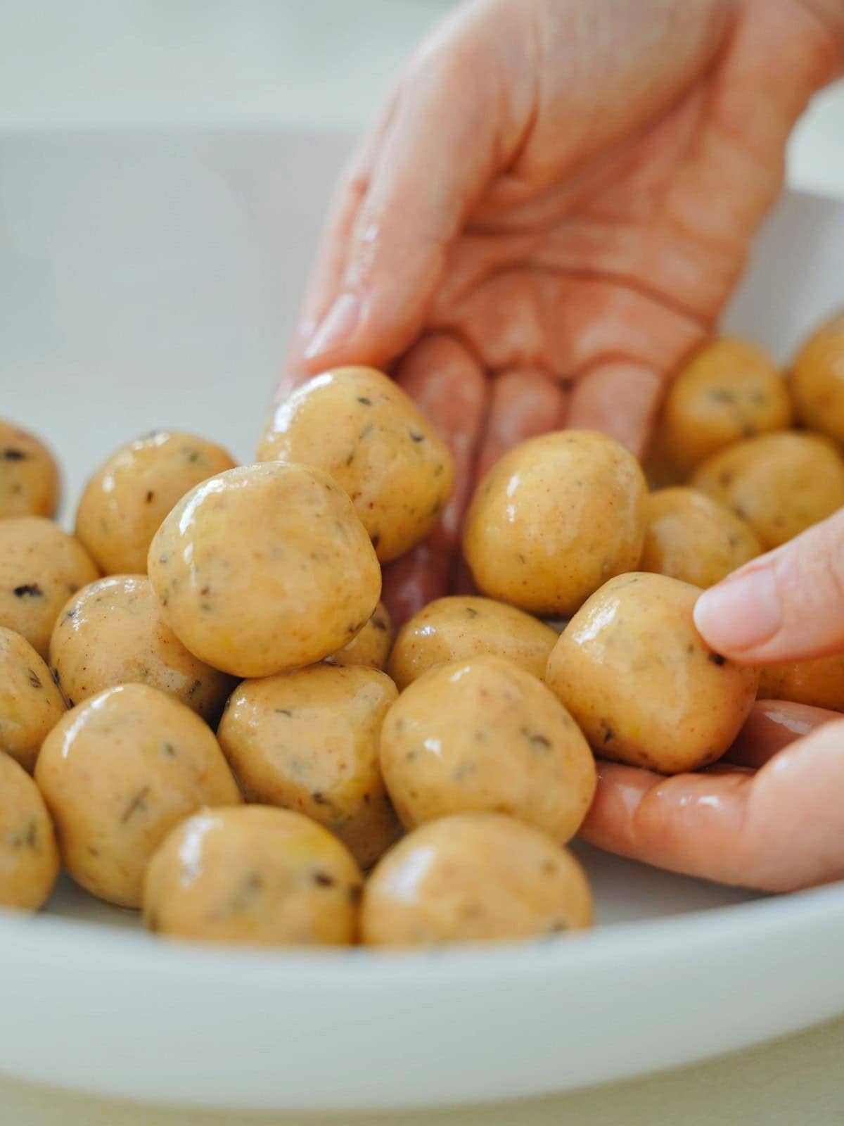 Hands shaping smooth, round potato dough balls in a white bowl