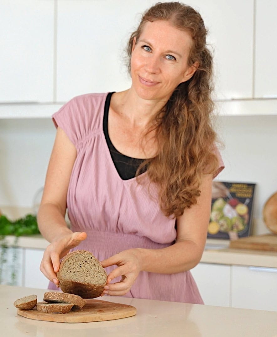 Michaela Vais smiling while holding a sliced loaf of bread on a wooden board