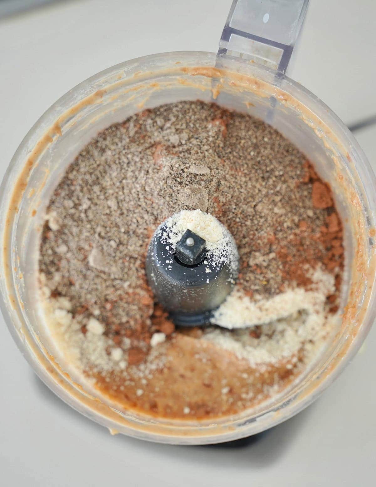 Top view of a food processor bowl filled with cocoa powder, almond flour, and chia seeds