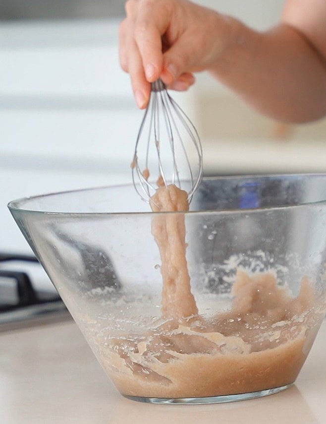 A hand holds a whisk lifting sticky psyllium gel from a glass bowl