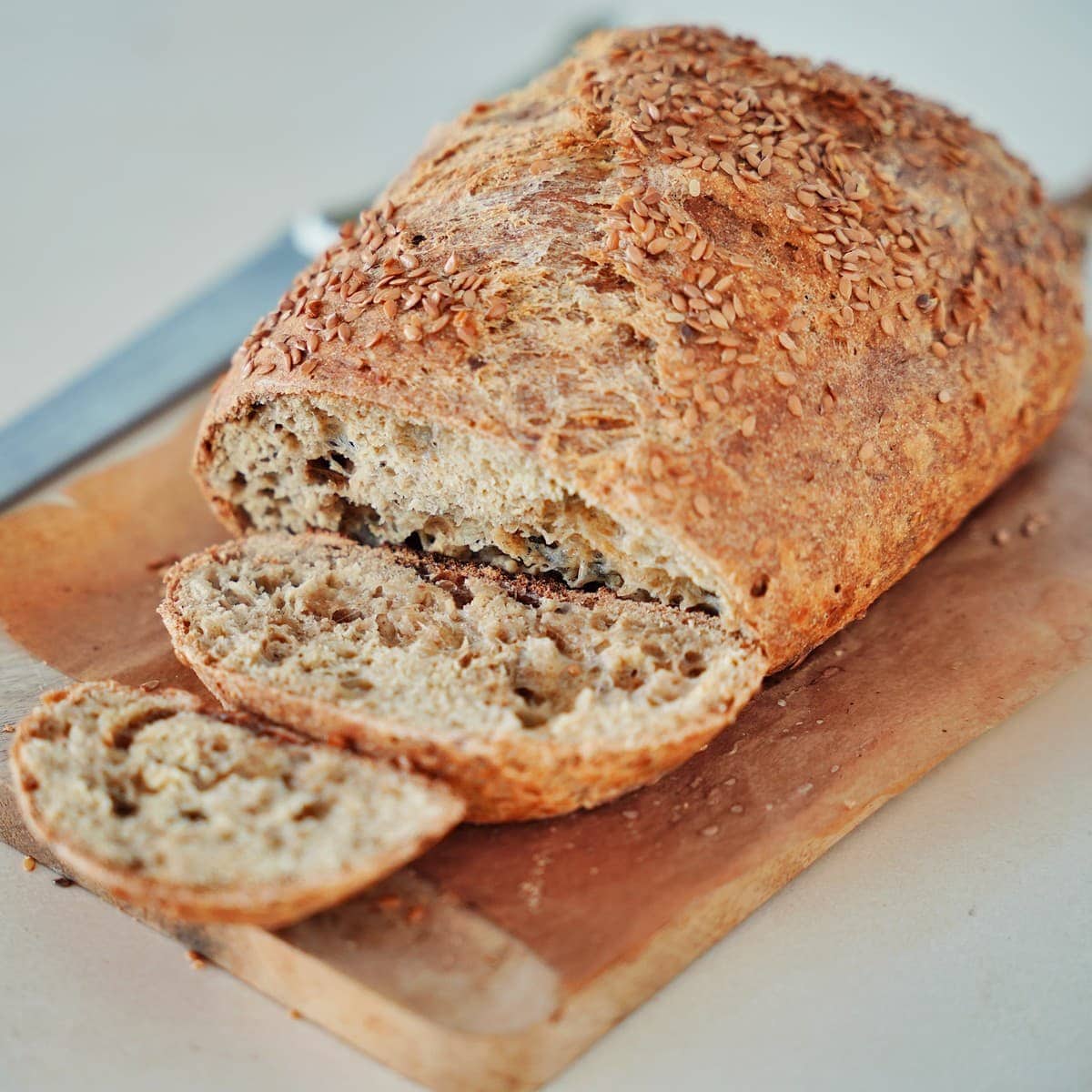 A rustic loaf of sliced chickpea flour bread with flax seeds on a cutting board