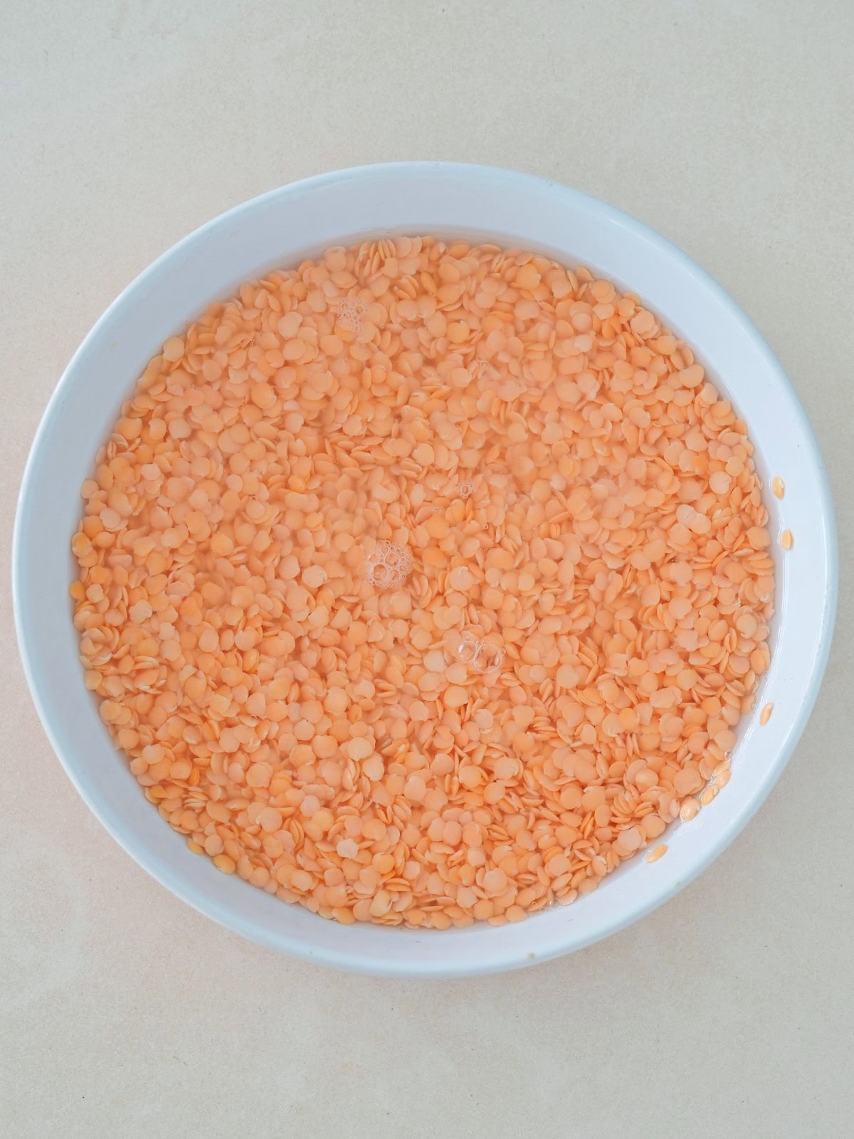 A white bowl filled with red lentils soaking in water