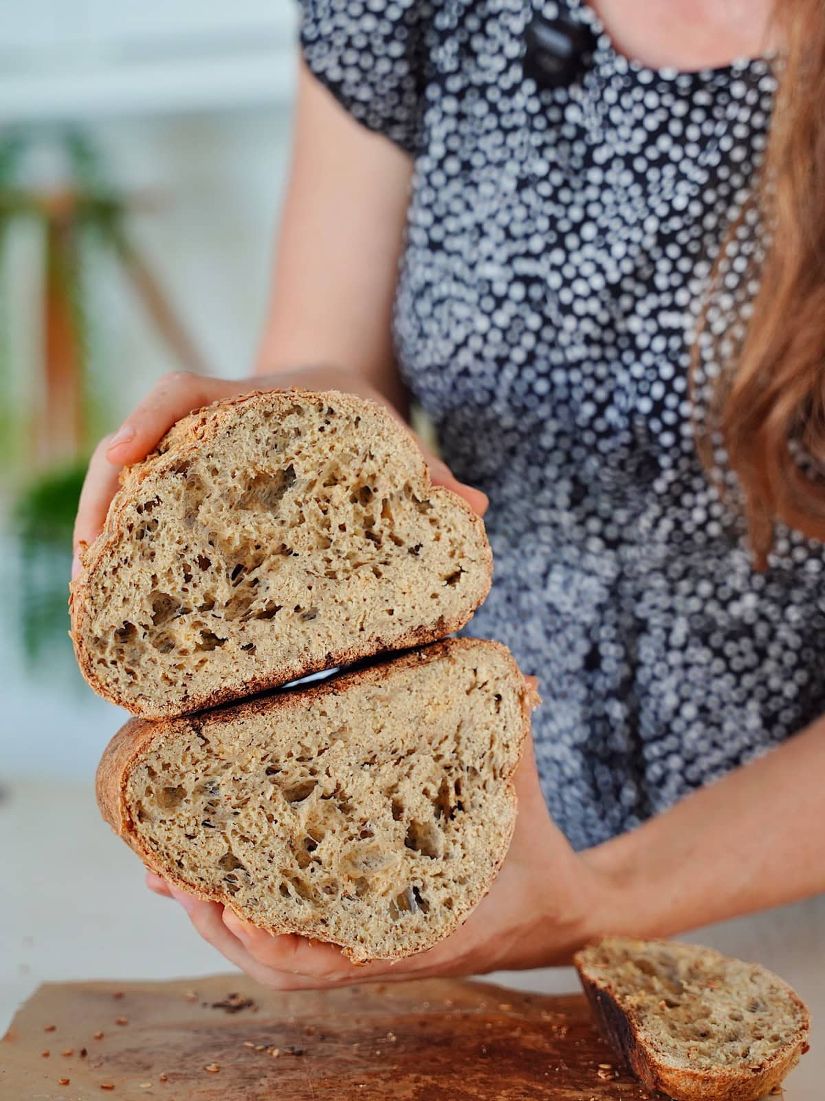 Elavegan in a patterned dress holds a loaf of rustic bread, sliced open
