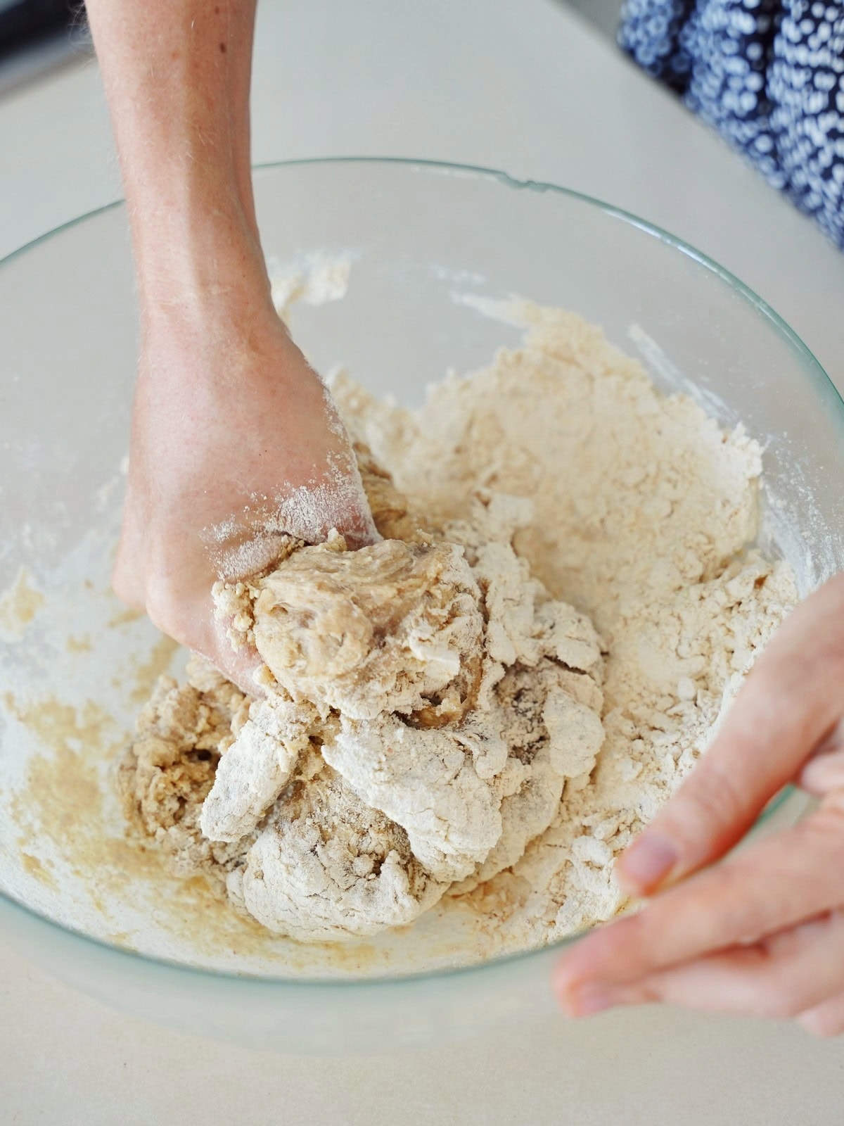 Hands kneading dough in a clear glass bowl