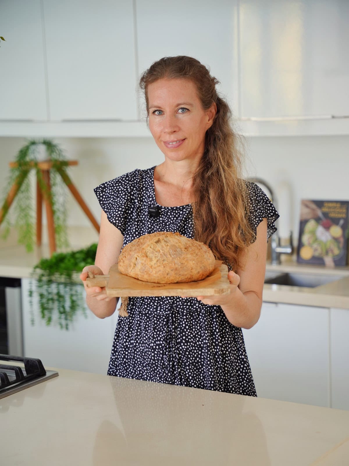 Michaela Vais in a polka dot dress holds a loaf of bread on a wooden board