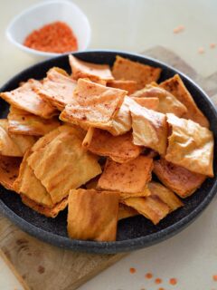A black bowl filled with crispy, golden-brown rectangular lentil crackers, dusted with paprika