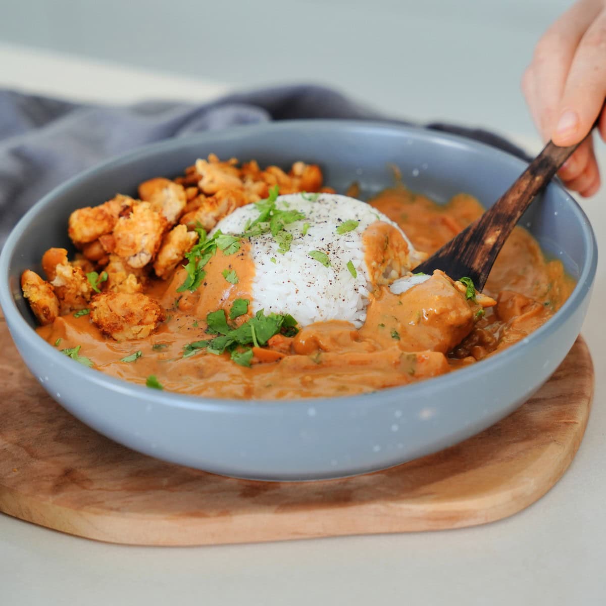 A bowl filled with creamy peanut curry, topped with rice and herbs, alongside crispy butter beans