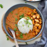 A gray bowl of creamy peanut curry with a mound of white rice, topped with pepper and cilantro