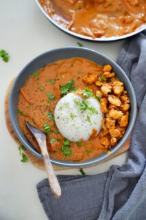 A gray bowl of creamy peanut curry with a mound of white rice, topped with pepper and cilantro