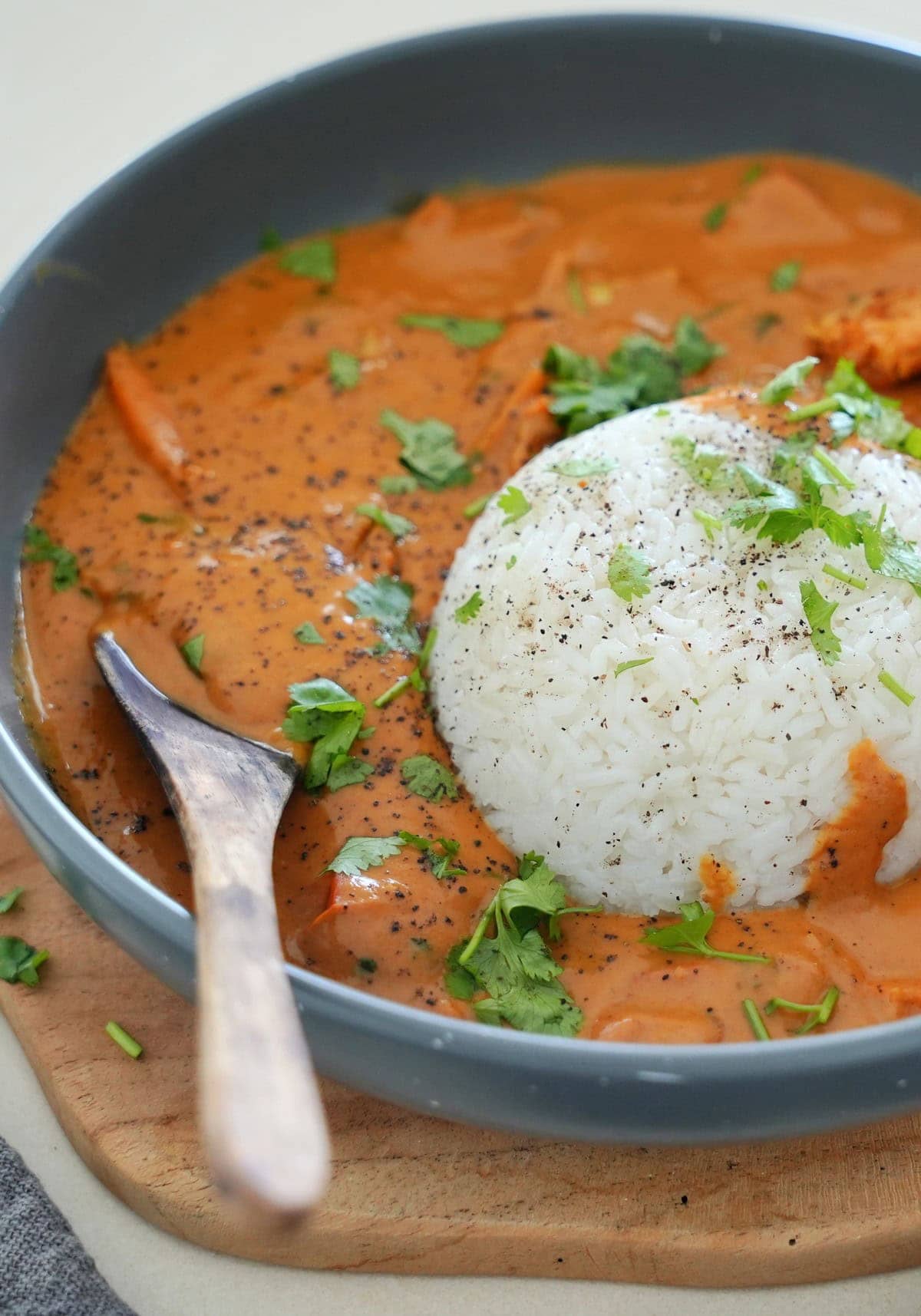 A grey bowl with rice topped with herbs, surrounded by creamy peanut curry and garnished with green cilantro