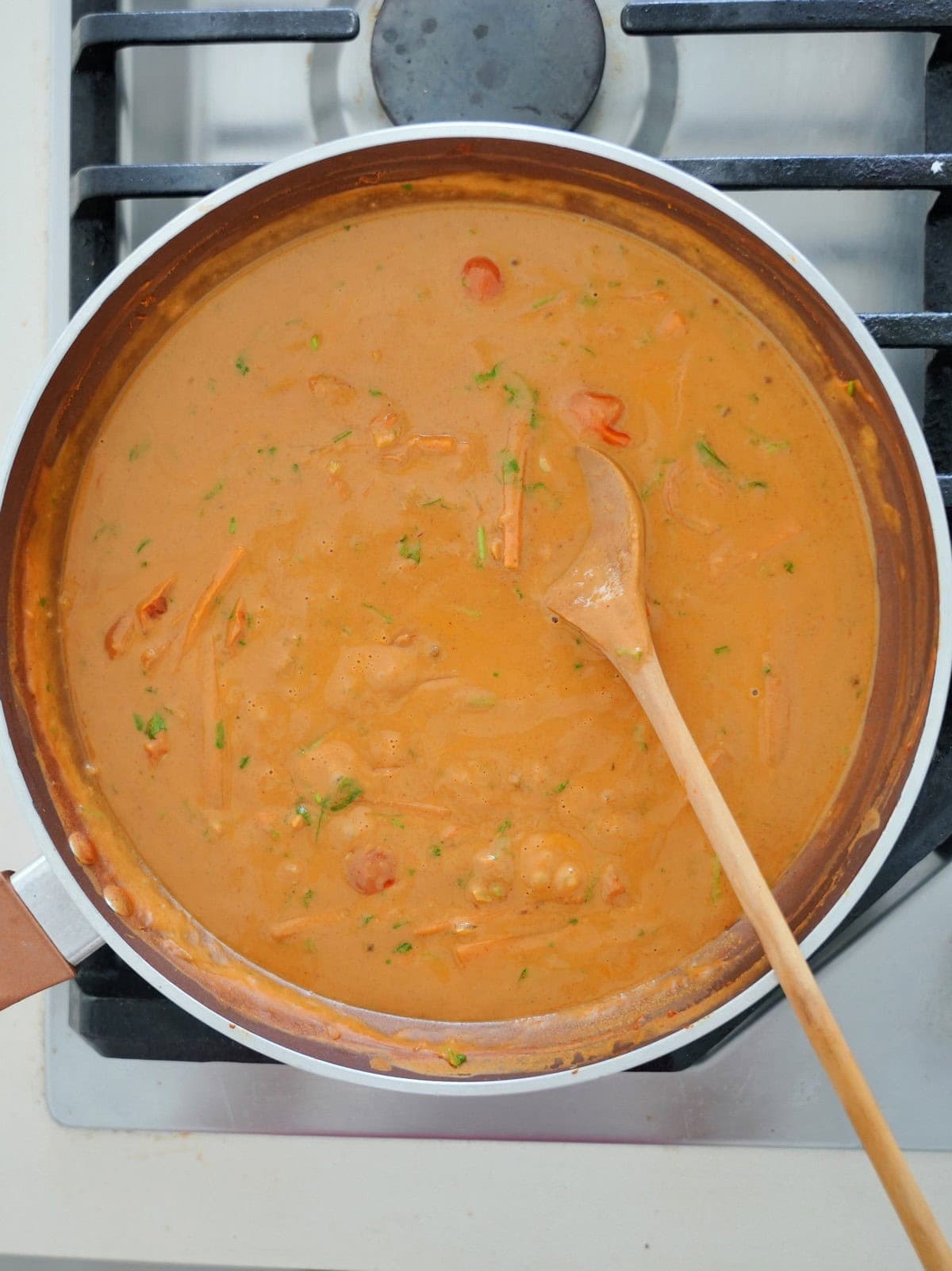 A saucepan with creamy orange curry on a stove, featuring visible chunks of vegetables and herbs