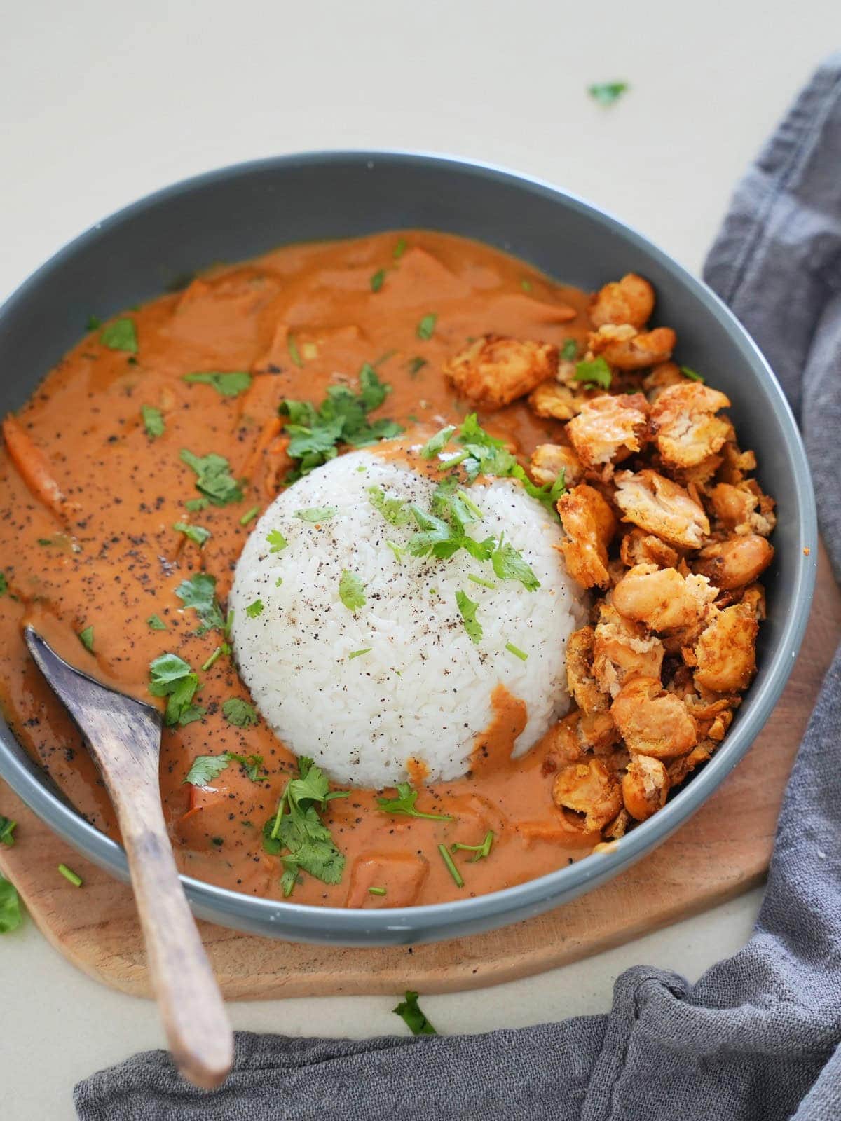 Bowl of creamy peanut curry with a mound of white rice, garnished with herbs, beside crispy butter beans
