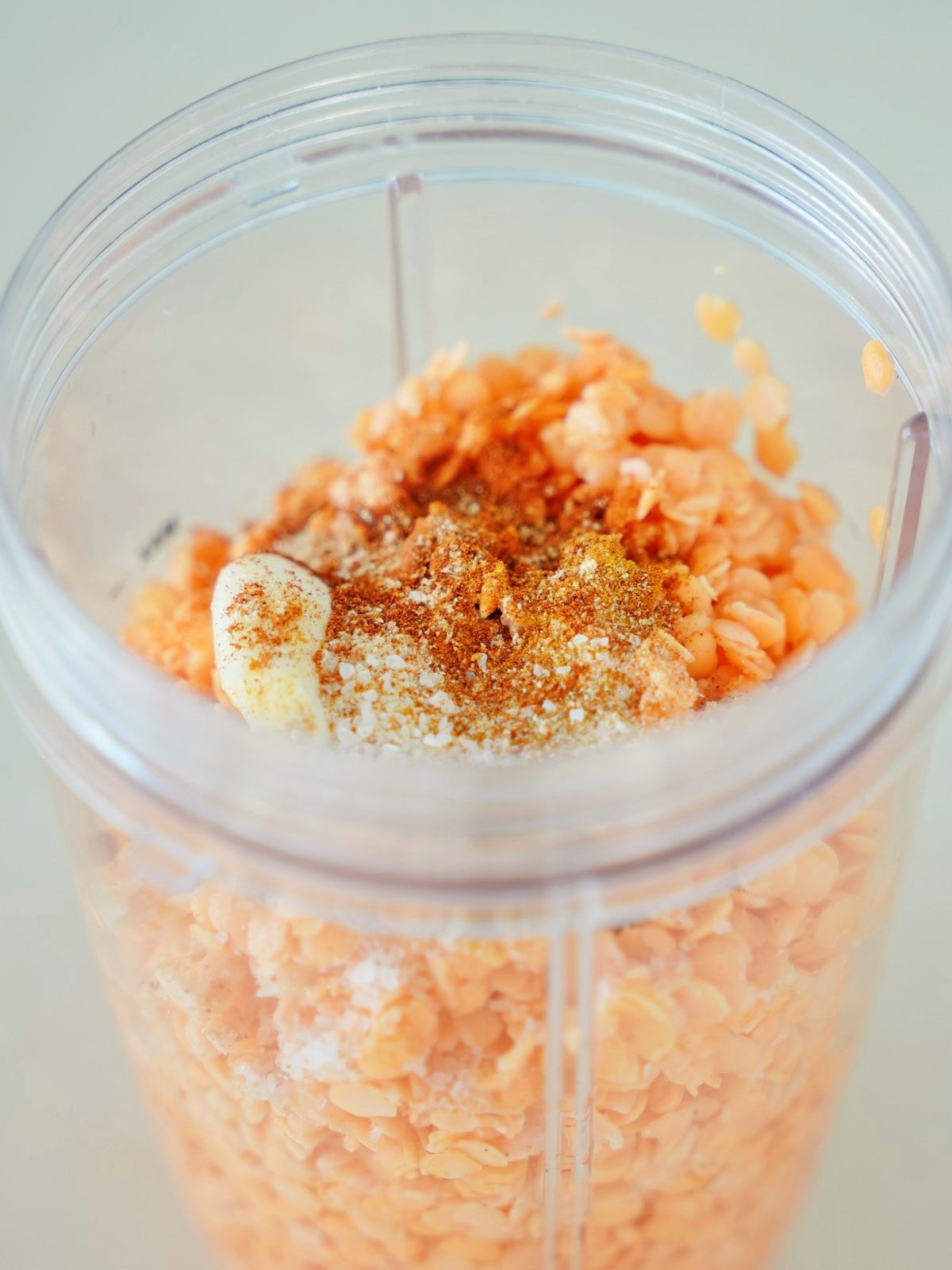 Close-up of red lentils in a blender cup, topped with spices and a clove of garlic