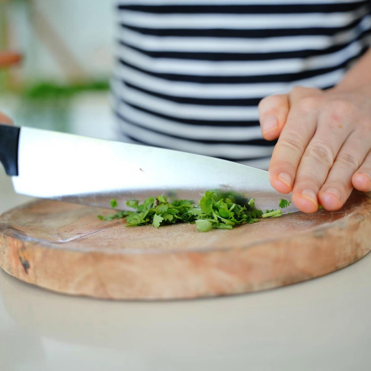 Elavegan chops fresh cilantro on a wooden cutting board with a large knife