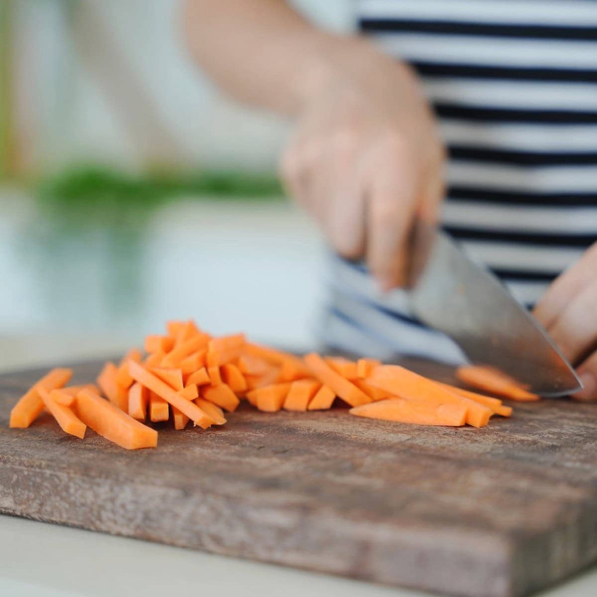 Elavegan slicing carrots into thin sticks on a wooden cutting board