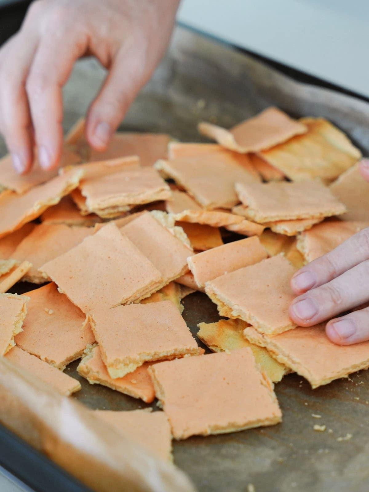 Hands arranging homemade crackers on a parchment-lined baking tray