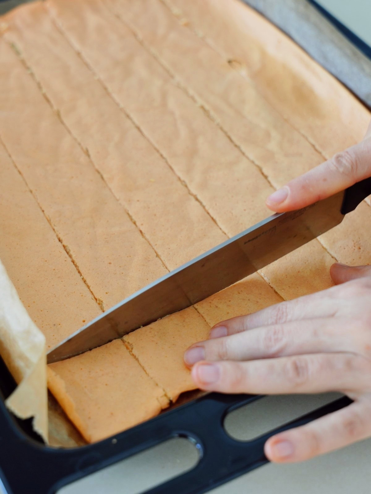Slicing a large rectangular cracker sheet on a tray into evenly sized strips using a knife