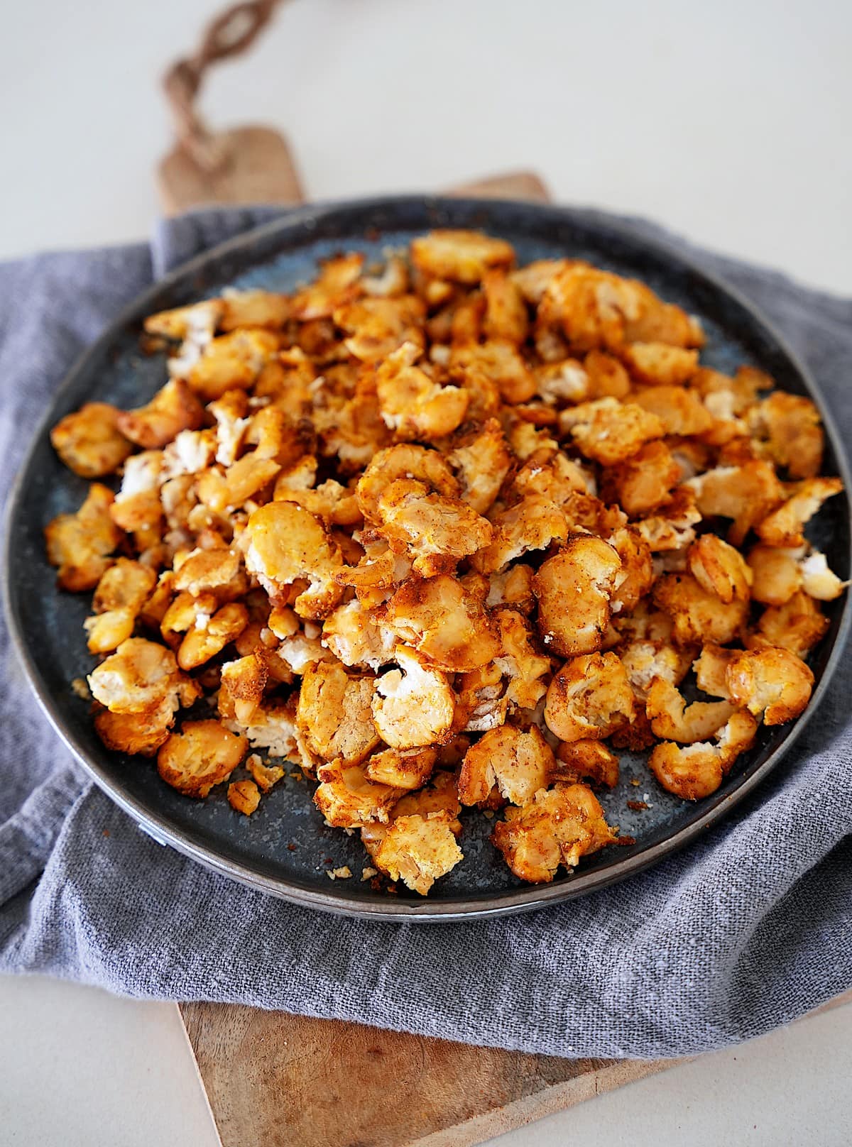 Auf einem grauen Tischtuch steht ein Teller mit goldbraun gerösteten, knusprigen Riesen-Bohnen