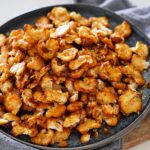A plate of crispy, golden-brown roasted butter beans on a dark plate, resting on a gray napkin