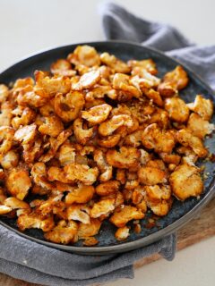 A plate of crispy, golden-brown roasted butter beans on a dark plate, resting on a gray napkin