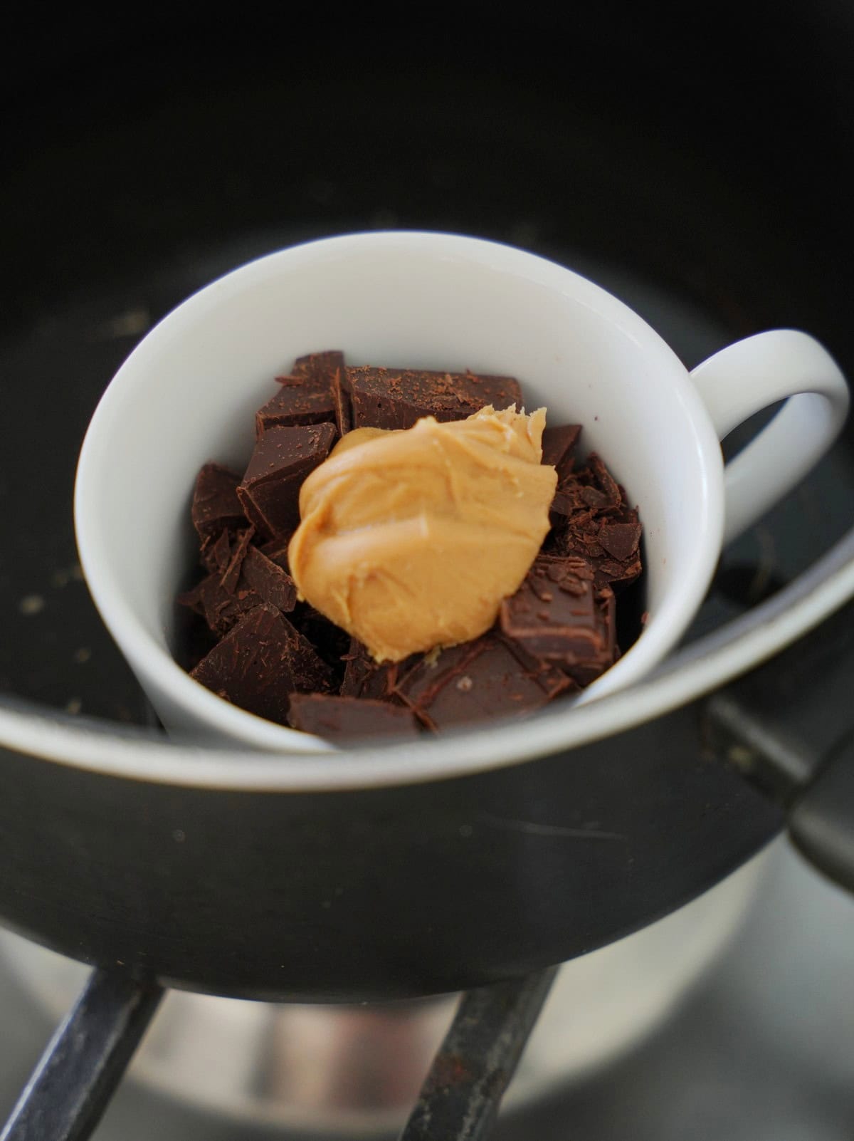 Eine weiße Tasse gefüllt mit gehackter Zartbitterschokolade und einem Klecks Erdnussmus 