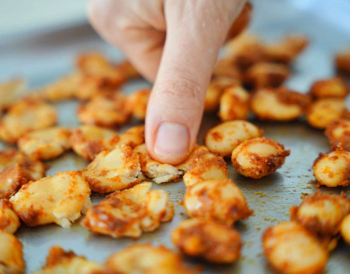 Nahaufnahme einer Hand, die goldbraune Riesenbohnen auf einem Backblech andrückt