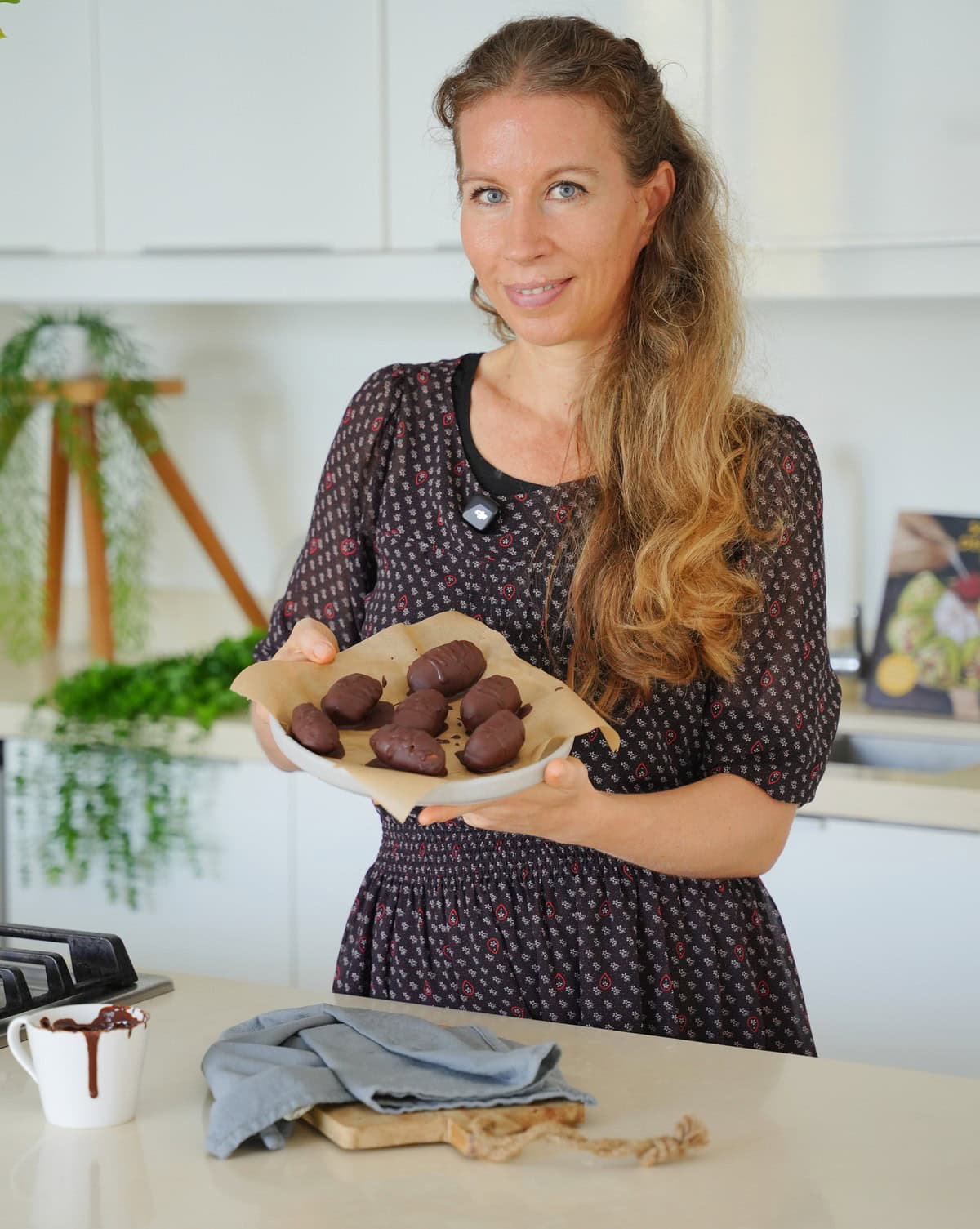 Michaela Vais in einer hellen Küche, hält einen Teller mit schokoladenüberzogenen Pralinen