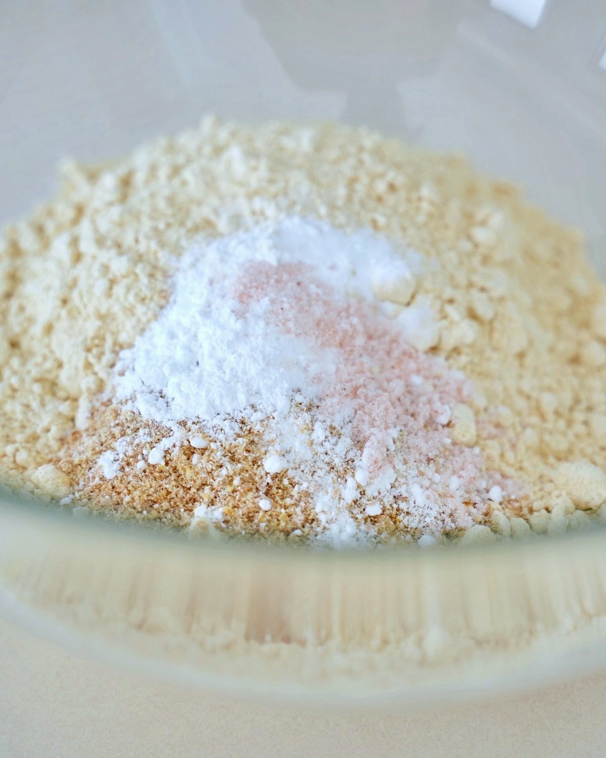 A close-up of a glass bowl containing a light yellow flour mixture with visible white and pinkish powder