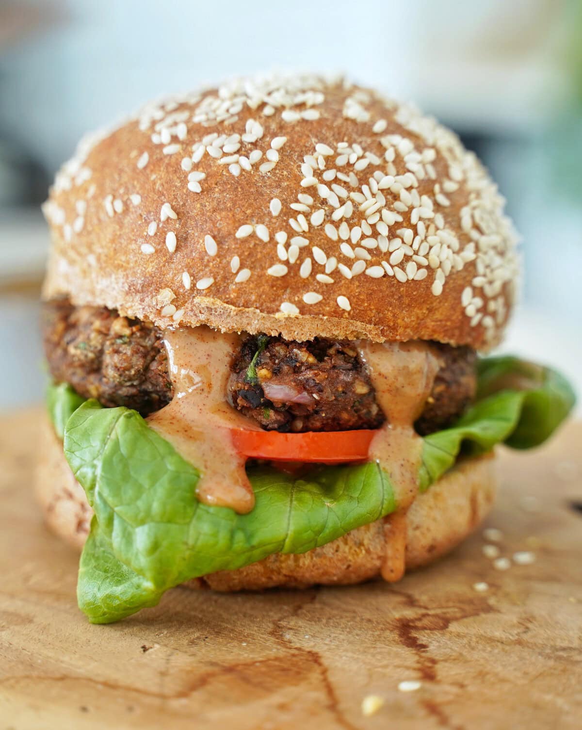 A close-up of a sesame seed bun burger with lettuce, a juicy patty, tomato slice, and a creamy sauce dripping