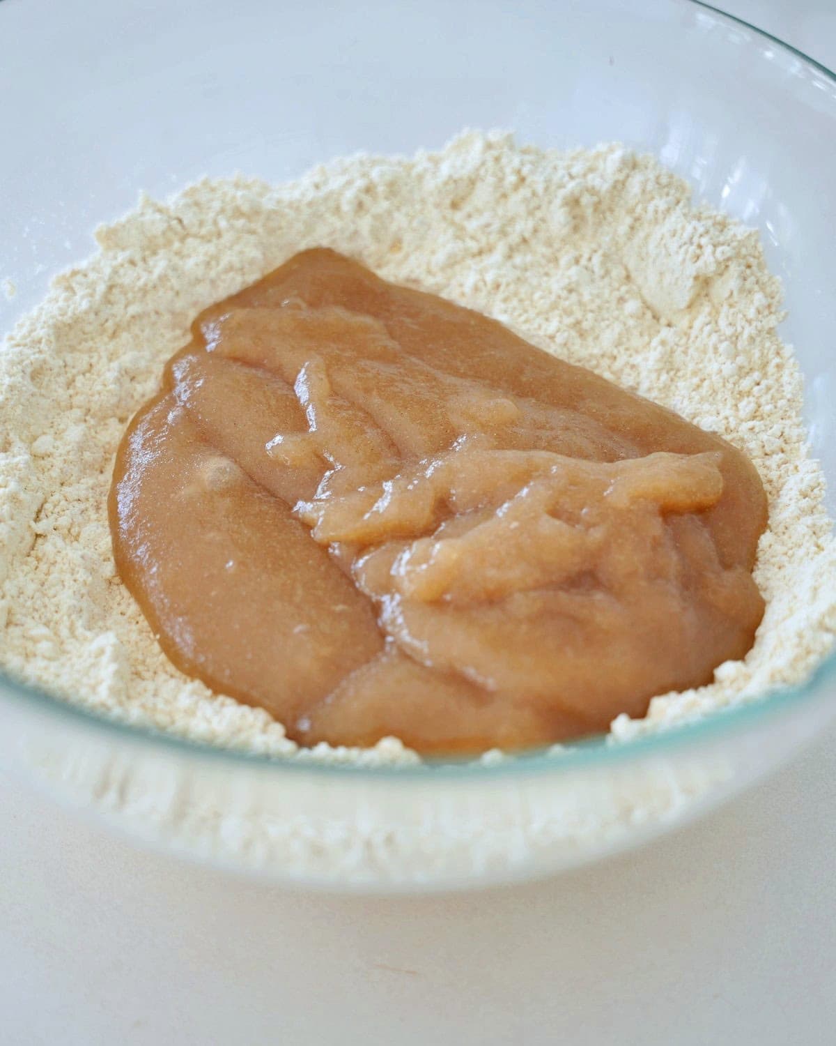 A glass bowl holds a mound of flour with a heap of psyllium gel in the center, ready to be mixed