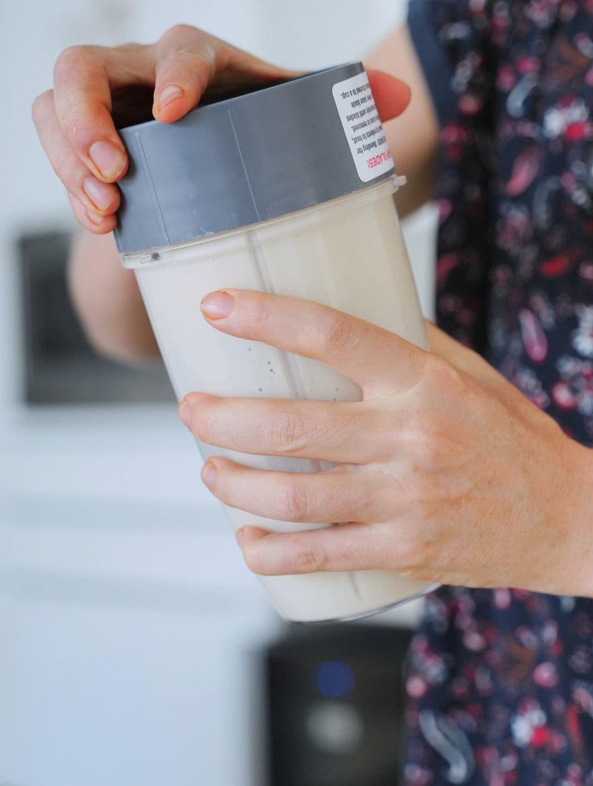 Close-up of hands holding a blender cup filled with a creamy white mixture