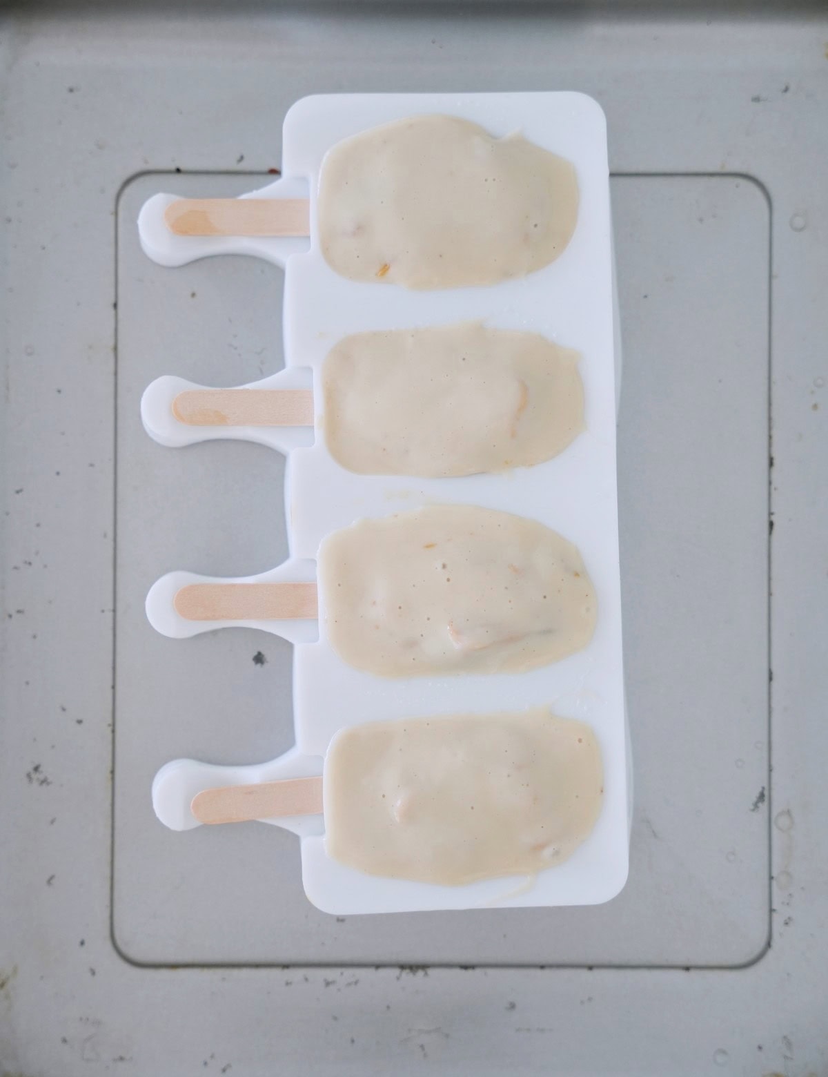 Four popsicles in a white mold filled with creamy, ivory-colored mixture. Wooden sticks protrude