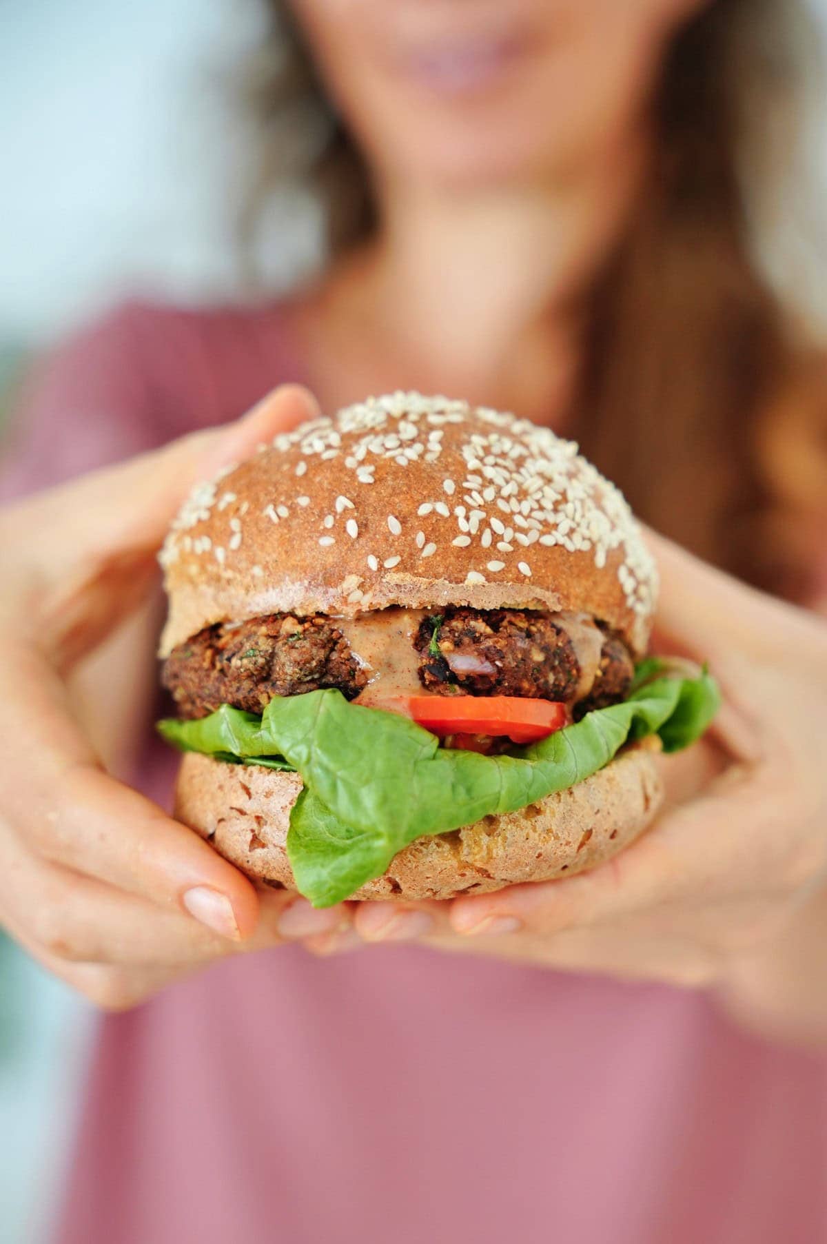 Michaela Vais holds a gluten-free sesame seed bun burger with lettuce, tomato, and a vegan patty