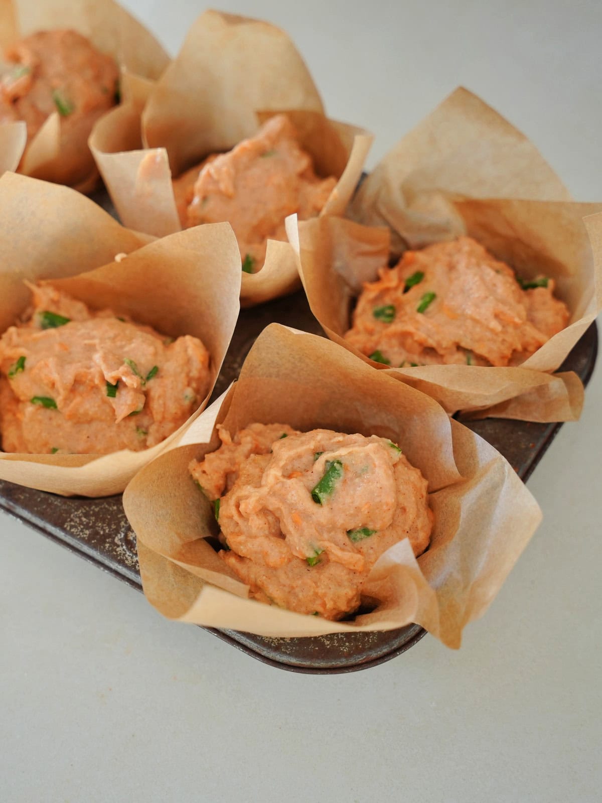 Muffinblech mit sechs rohen herzhaften Muffins in braunen Backförmchen