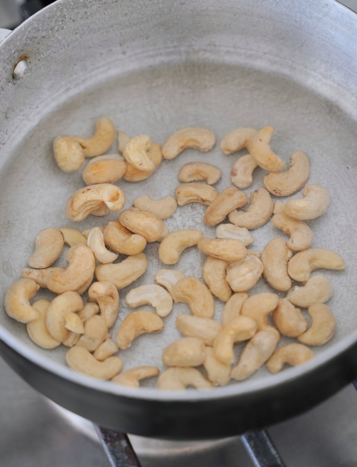 Raw cashews scattered in a silver frying pan