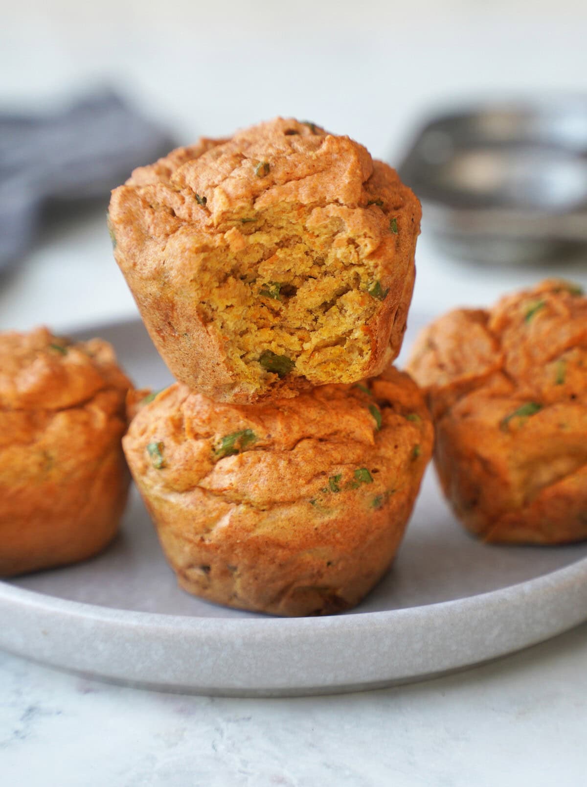 Auf einem grauen Teller liegen 2 herzhafte Muffins übereinander. Von einem Muffin ist ein Stück abgebissen.