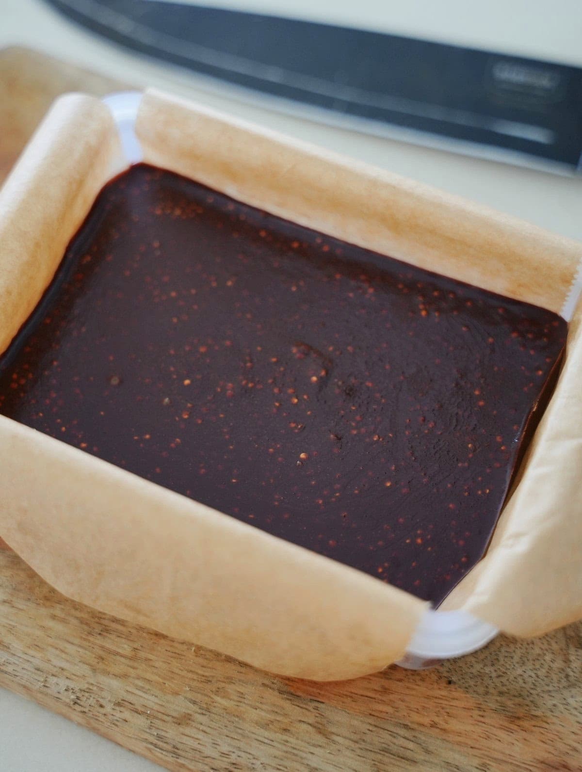A rectangular container lined with parchment paper filled with dark quinoa chocolate placed on a wooden surface