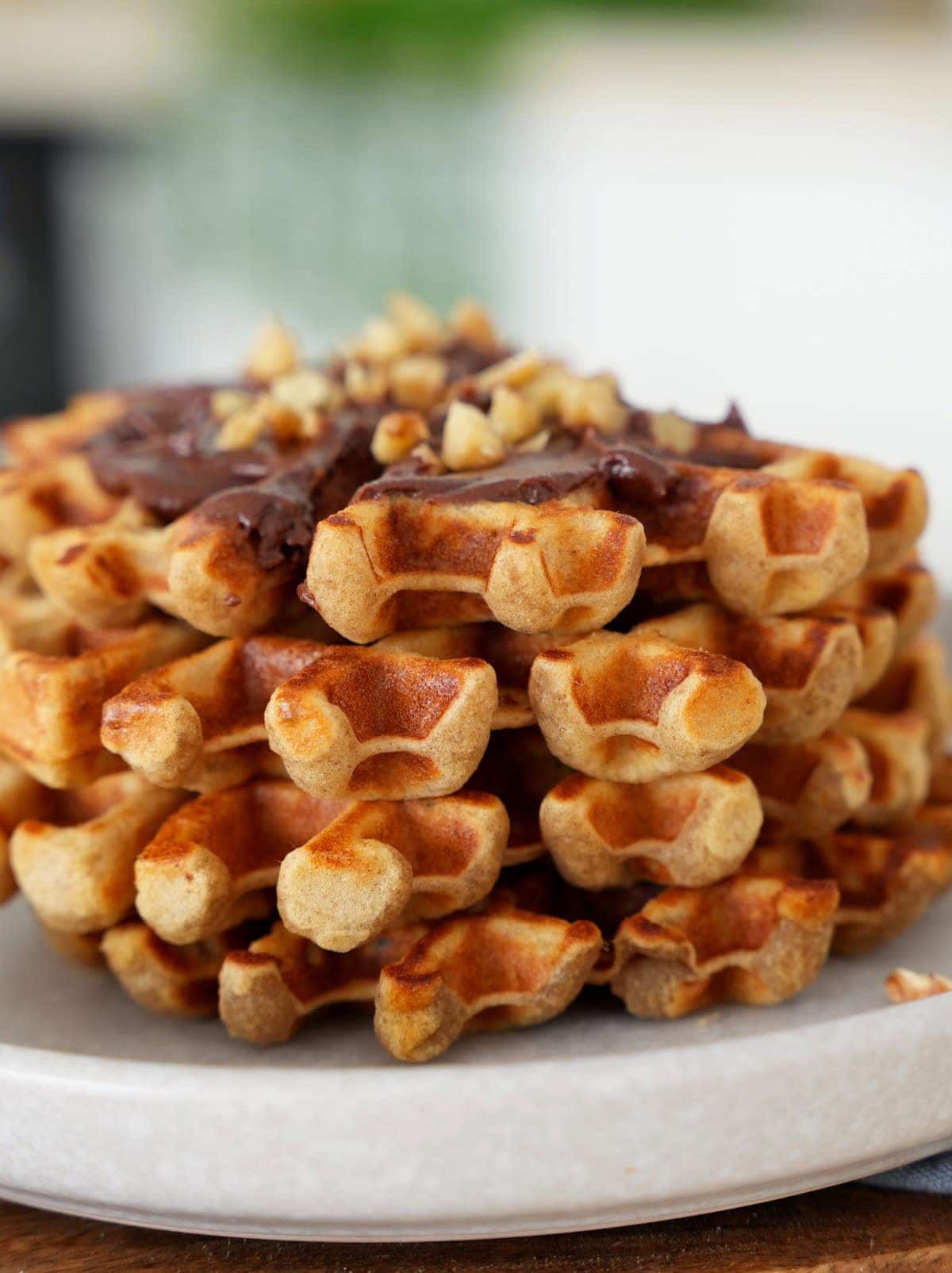 A close up stack of golden brown waffles topped with chocolate spread and chopped nuts