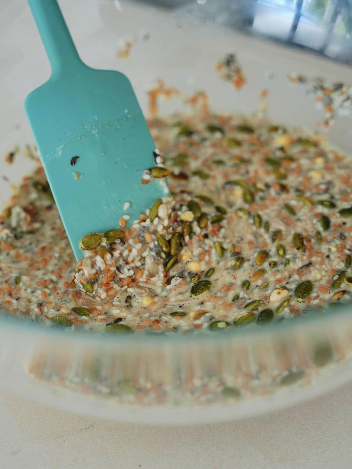 A turquoise spatula mixing a blend of seeds in clear glass bowl