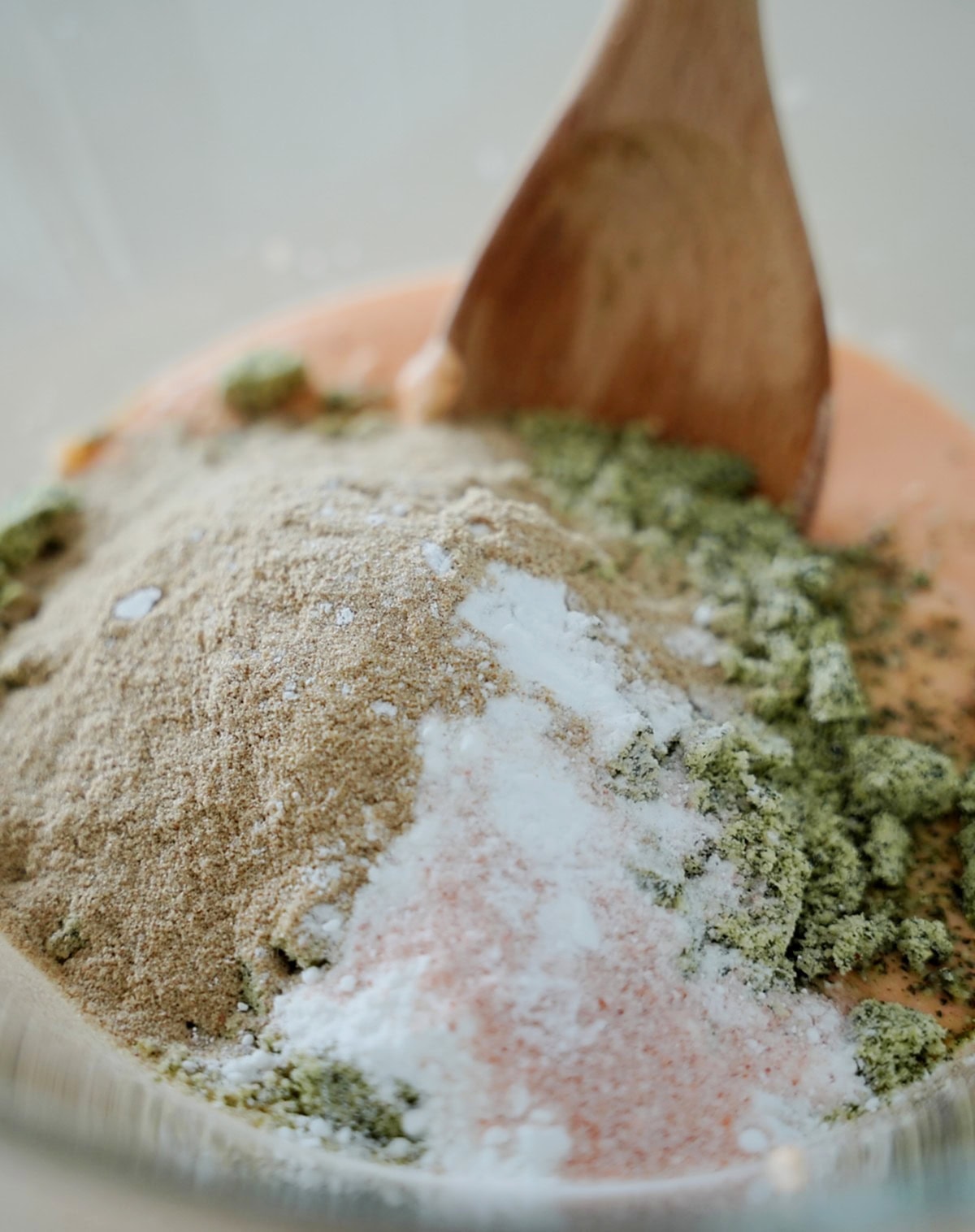 Close-up of various dry ingredients in a mixing bowl, including psyllium, salt, and ground pumpkin seeds, with a wooden spoon.