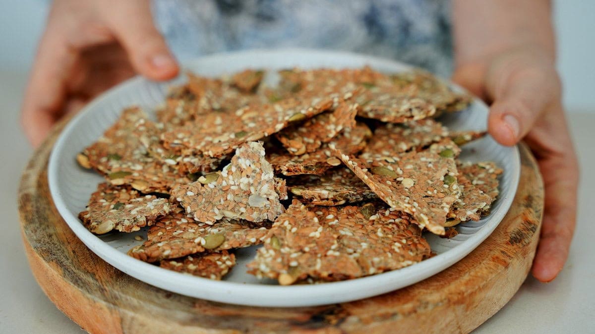 Hands holding a plate filled with crispy multi-seed crackers