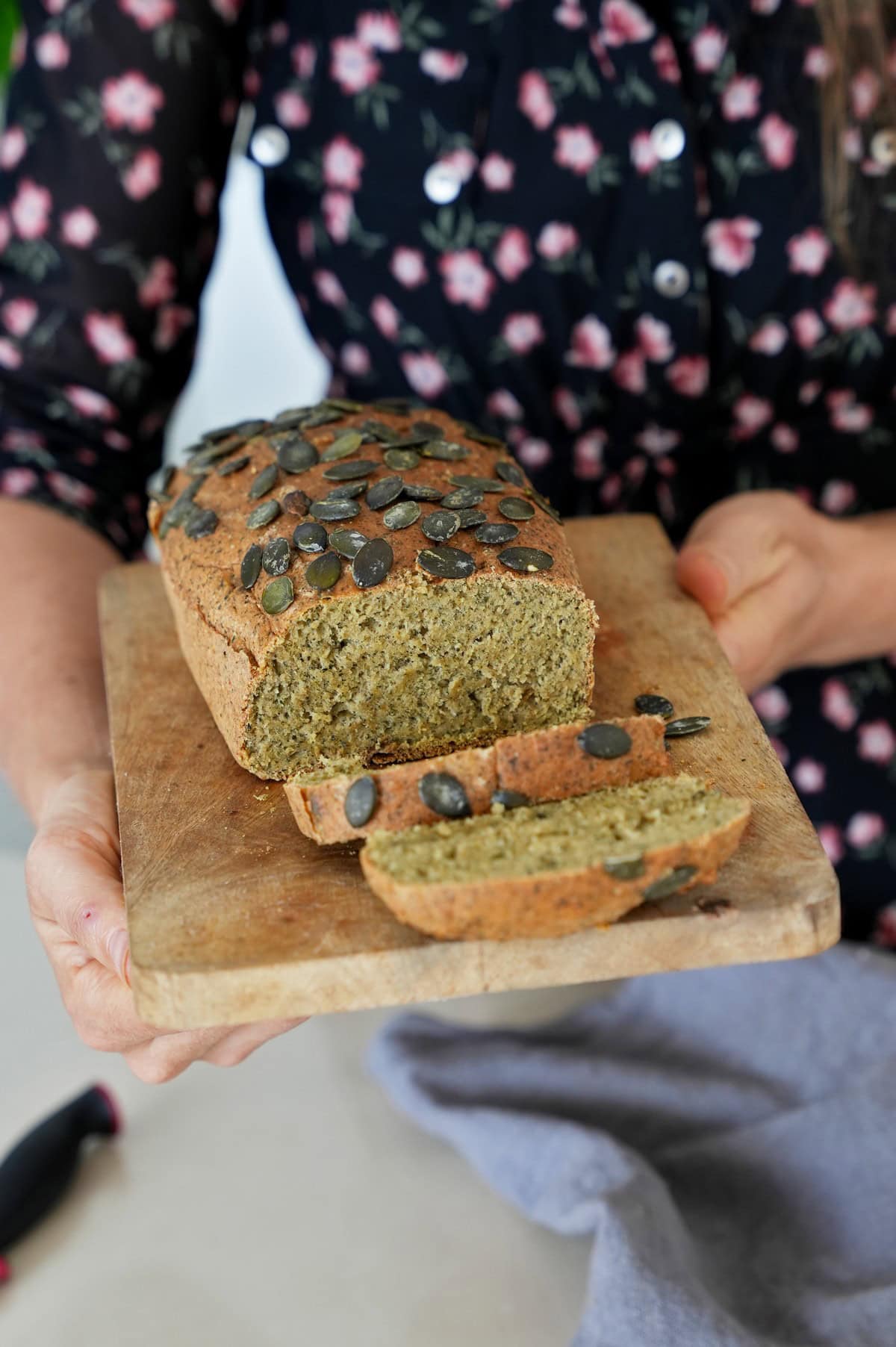 Hands holding sliced lentil bread topped with pumpkin seeds on wooden board.