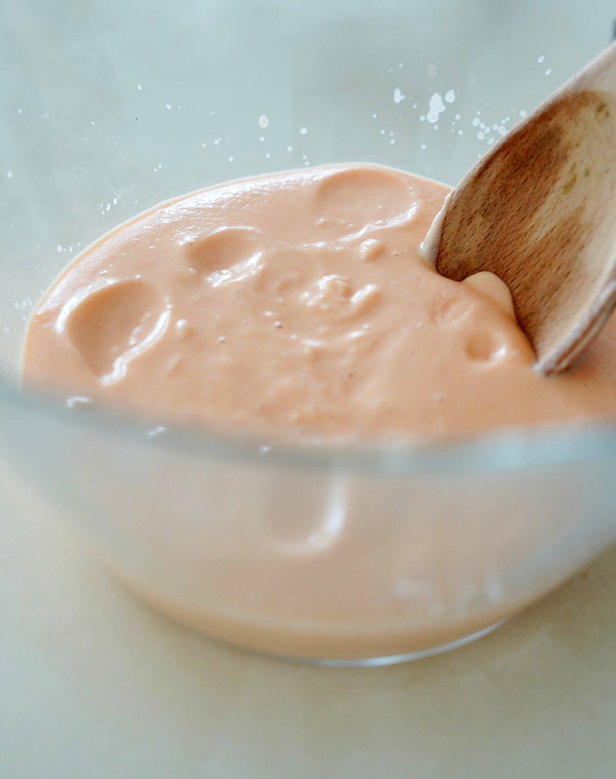 Red lentil batter in a glass bowl with a wooden spoon.