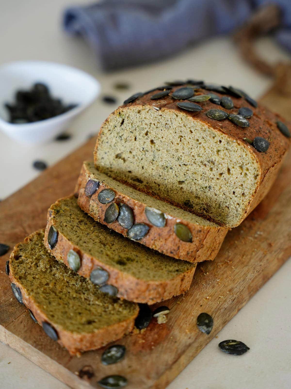 Sliced red lentil bread topped with pumpkin seeds on wooden board