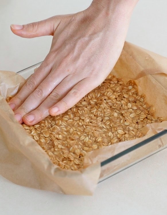 hands pressing oat pb mixture into glass pan