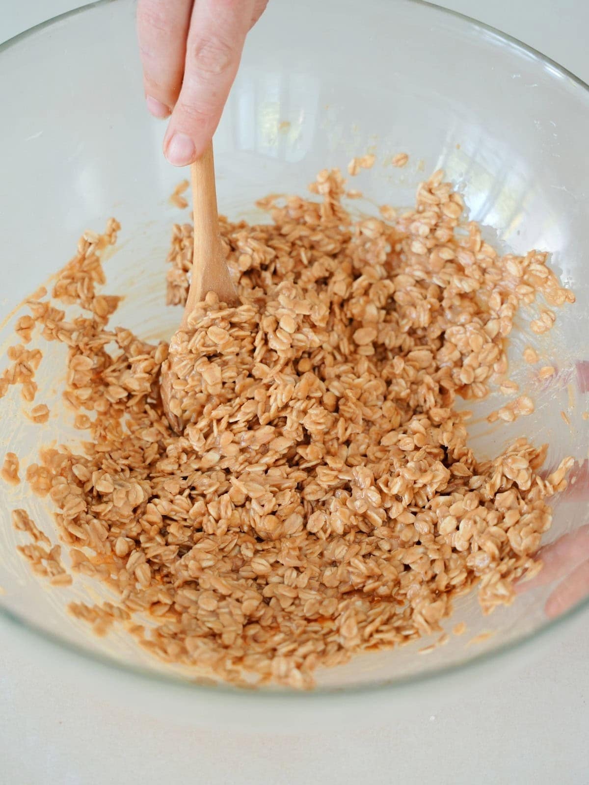 mixing oats with peanut butter with wooden spoon in glass bowl.