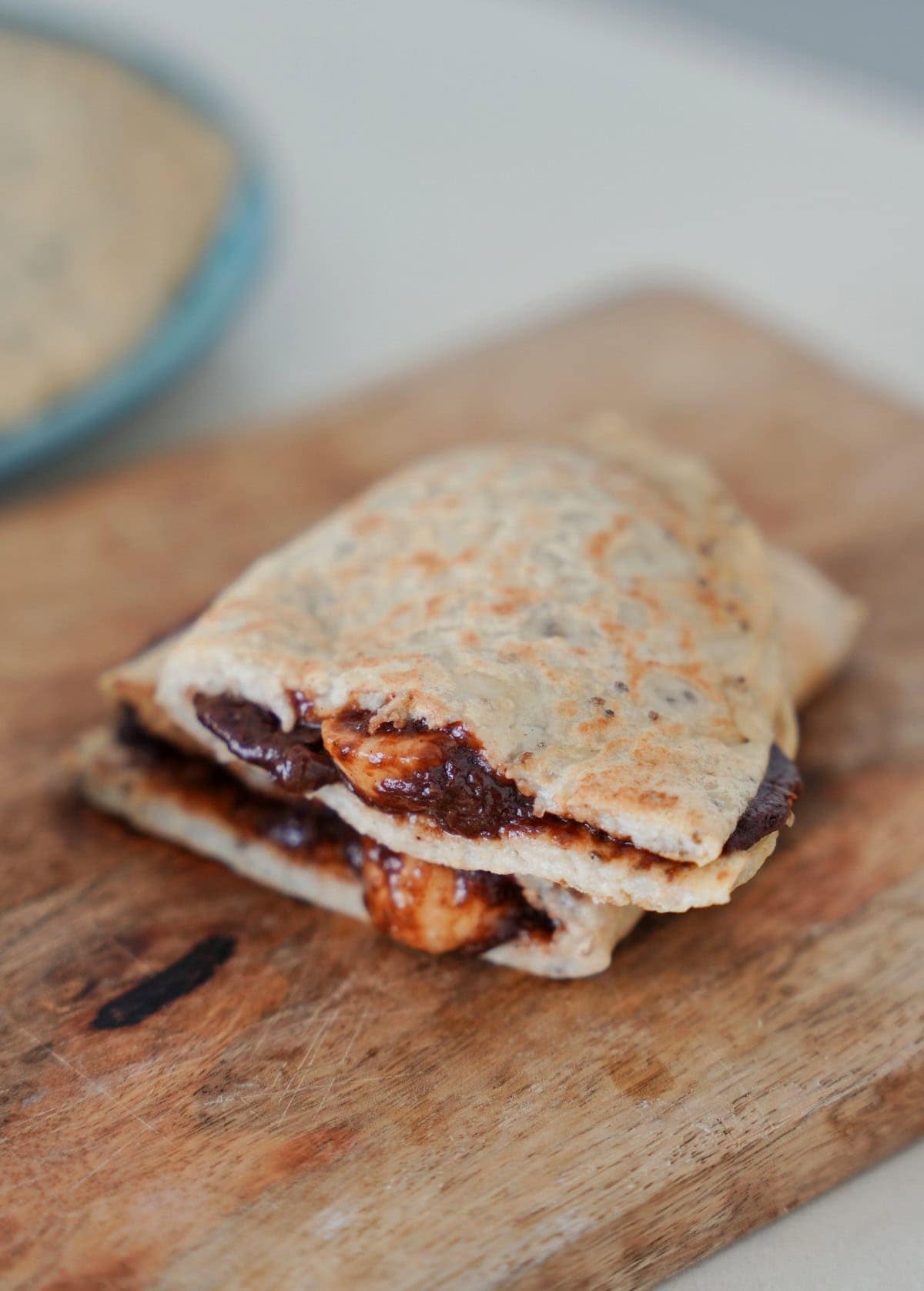 A folded oat wrap filled with melted chocolate and sliced bananas rests on a rustic wooden cutting board