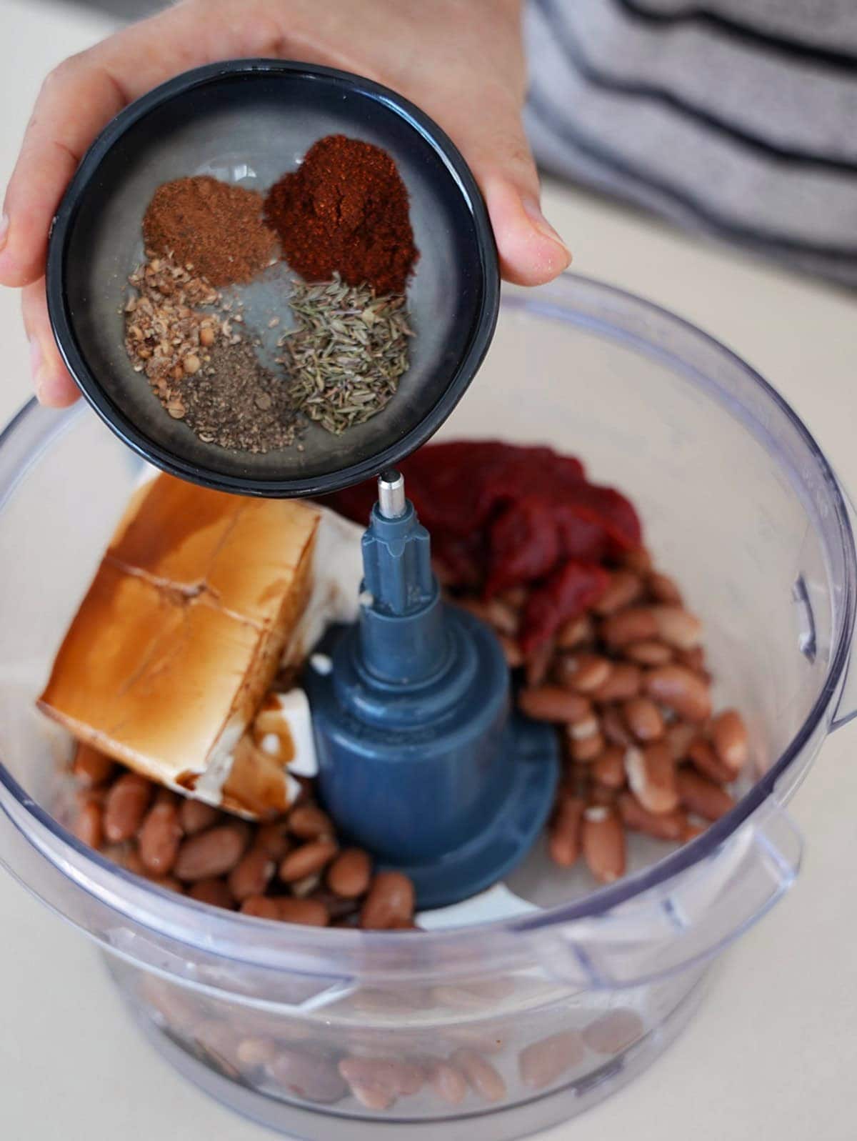 Adding spices to food processor containing tofu and beans.